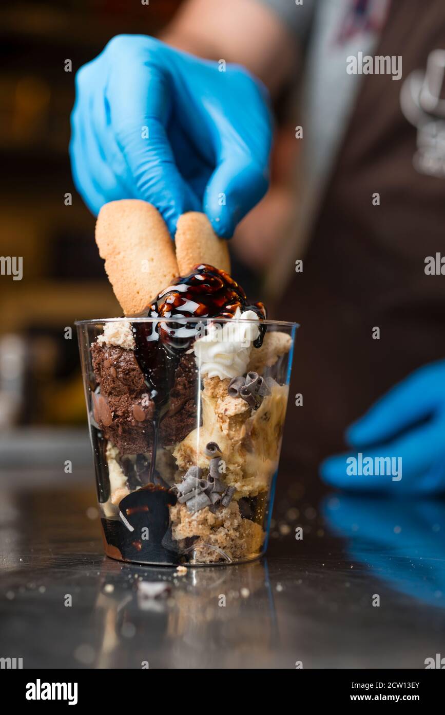 Préparation artisanale d'une tasse de verre de noix et de grains, glace italienne glace glace glace glace à la crème fouettée et biscuits à la langue du chat. Banque D'Images