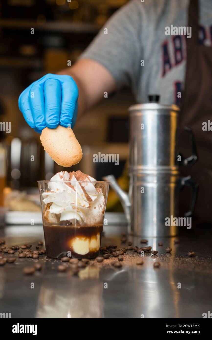 Préparation artisanale d'une tasse de glace italienne glace glace galato affogato noyée dans un café expresso avec de la crème fouettée et des biscuits à la langue du chat. Banque D'Images