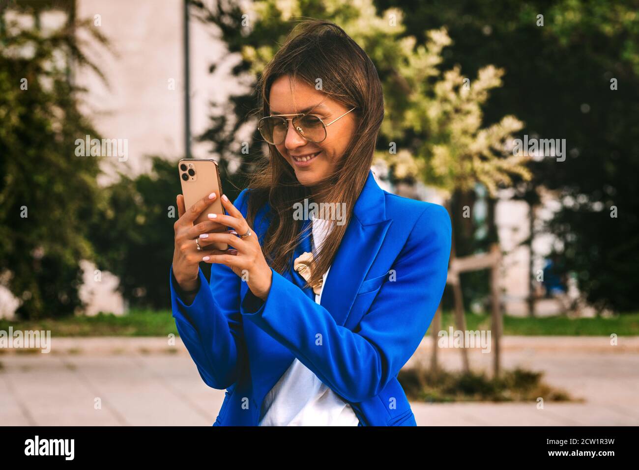 Femme d'affaires souriante dans un blazer bleu tenant un smartphone. Saisie du message. Envoi de SMS Banque D'Images
