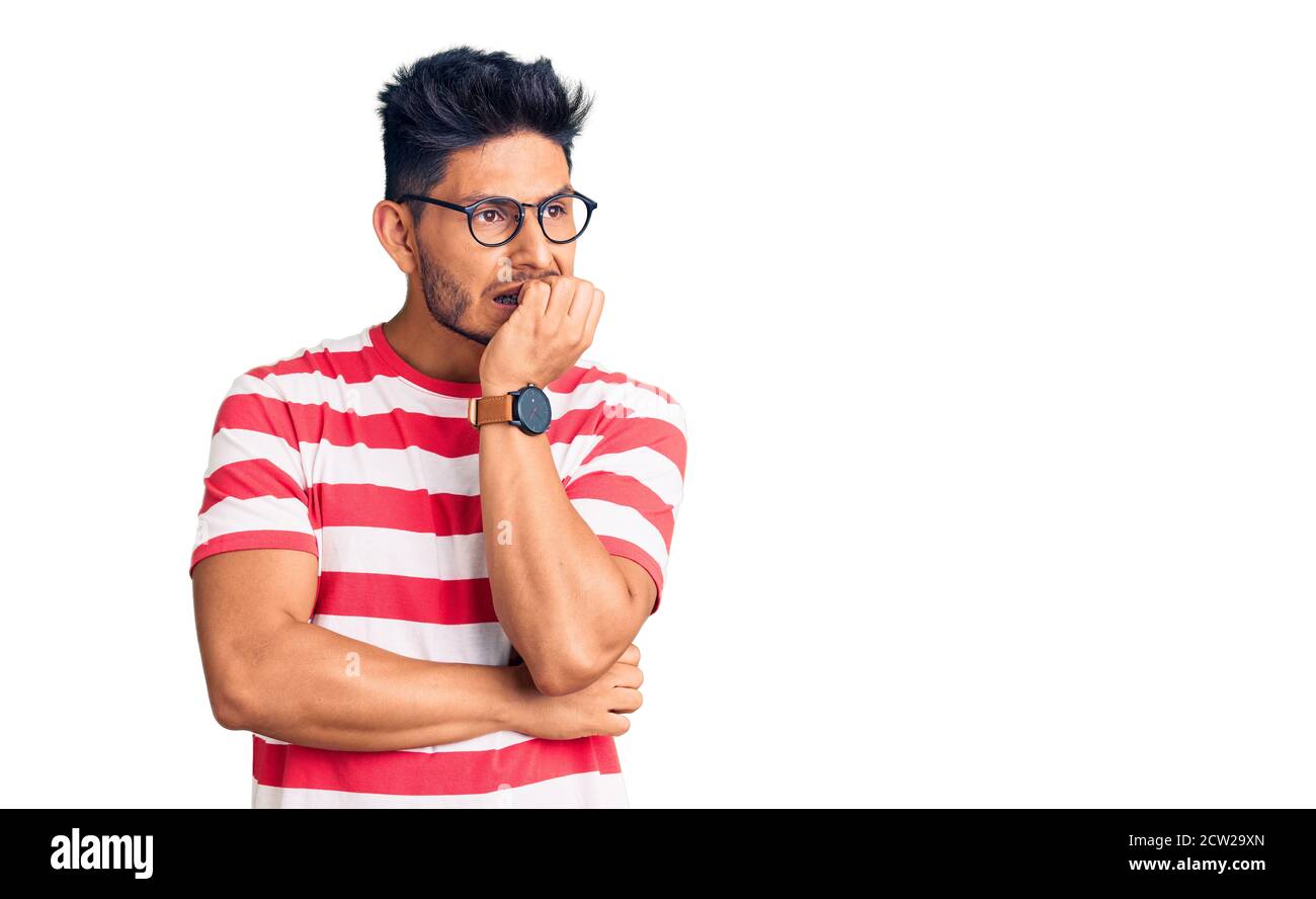 Beau jeune homme latino-américain portant des vêtements et des lunettes décontractés, il a l'air stressé et nerveux avec les mains sur la bouche piquant les ongles. Banque D'Images