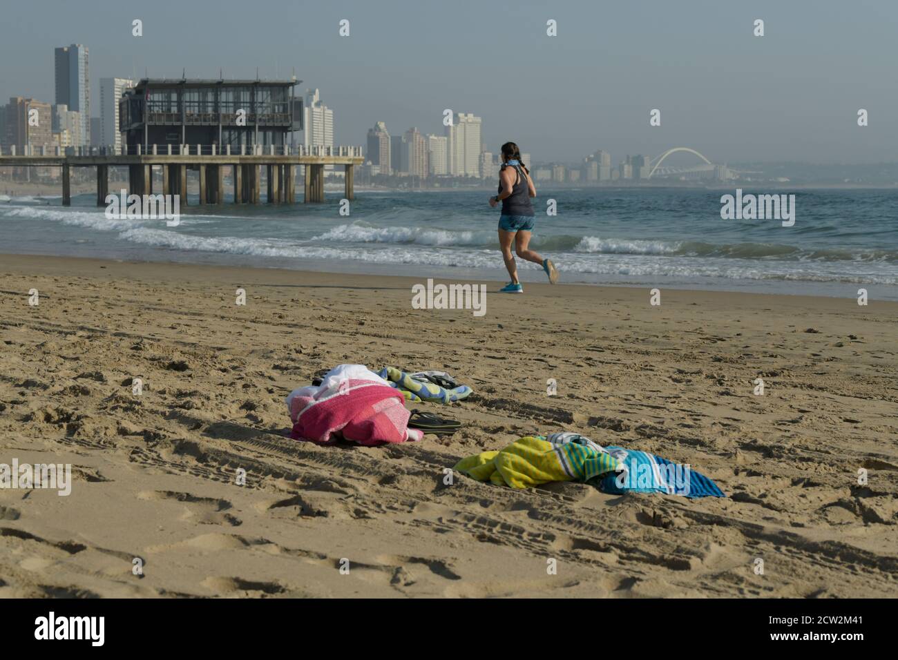 Femme adulte courant sur la plage, Durban, KwaZulu-Natal, Afrique du Sud, activité en bord de mer, entraînement, paysage, ville, jetée Ushaka, front de mer, serviettes Banque D'Images