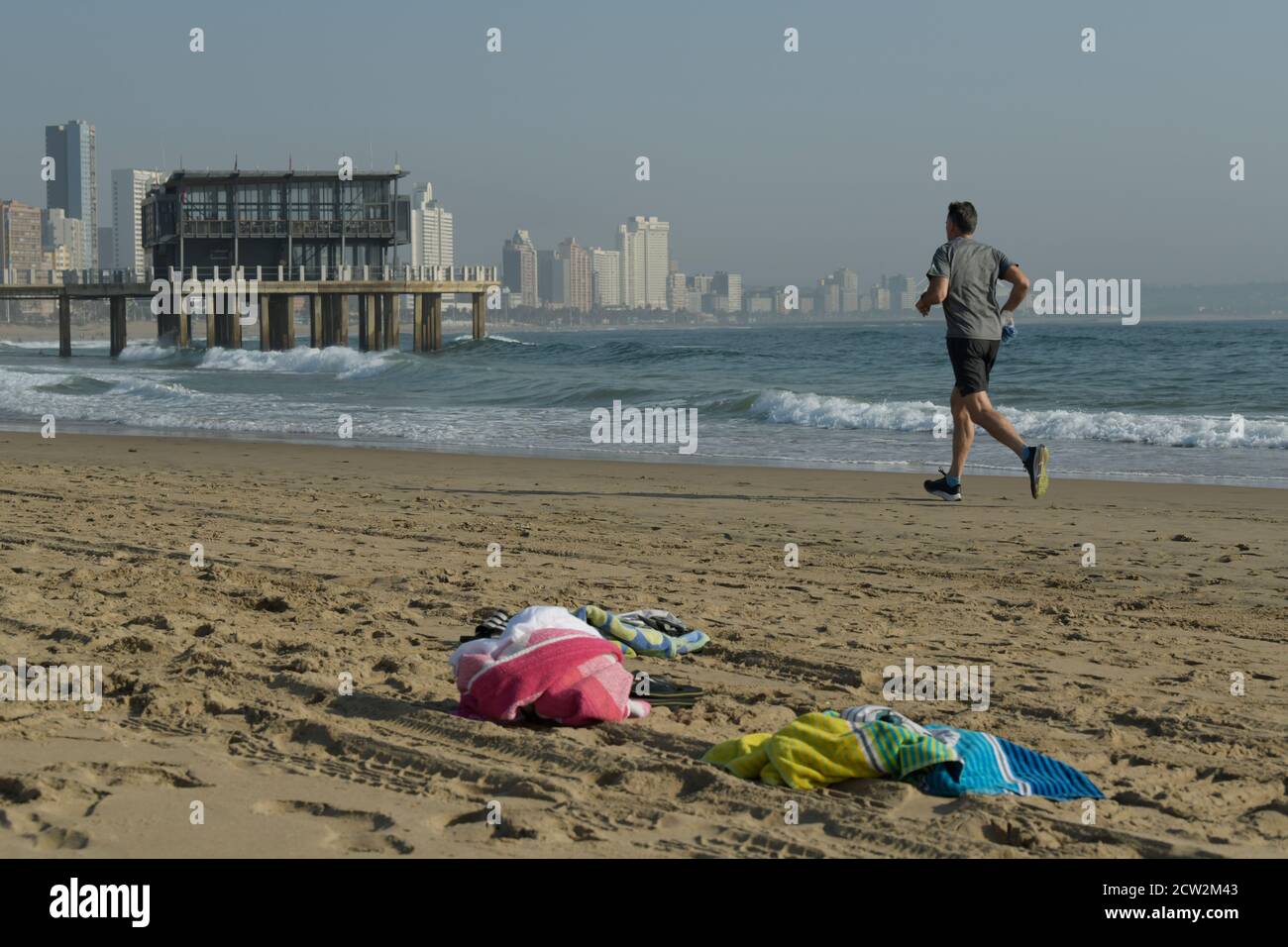 Homme adulte courant sur la plage, Durban, KwaZulu-Natal, Afrique du Sud, activité en bord de mer, entraînement, paysage, ville, front de mer, jetée Ushaka, serviettes, voyage Banque D'Images