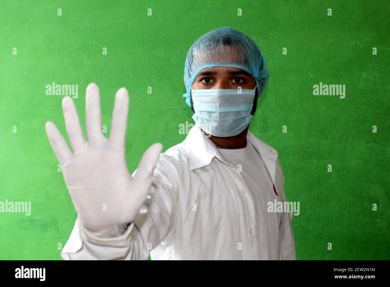 Un jeune médecin en uniforme médical avec un masque facial protecteur et une main gantée montrant un signe d'arrêt - Stop corona virus, Covid-19 concept. Banque D'Images