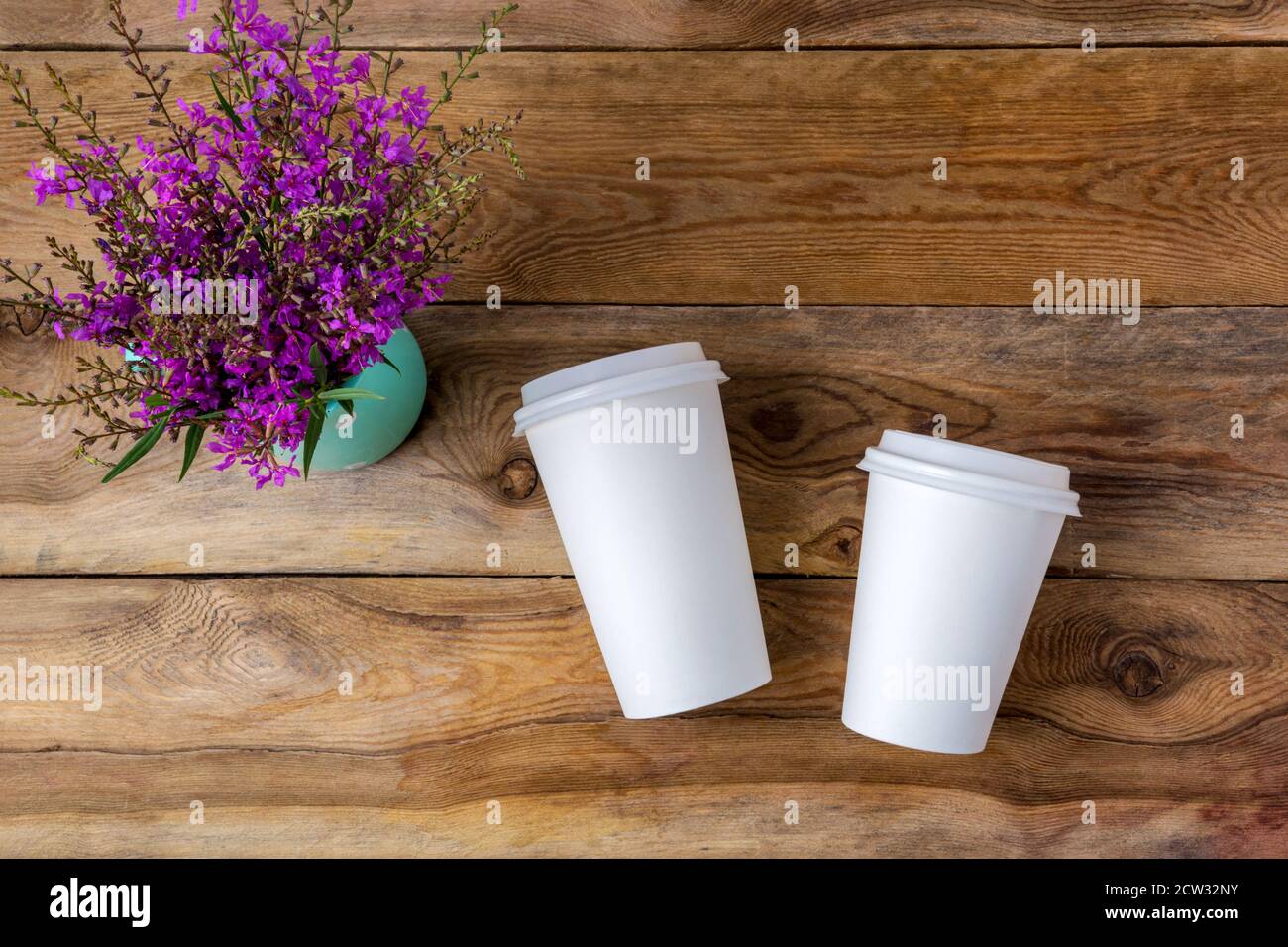 Tasse en papier chaud jetable avec café blanc et couvercle, effet de maquette avec fleurs sauvages violettes. Tasses à café en plastique avec couvercles pour la promotion du design. Banque D'Images