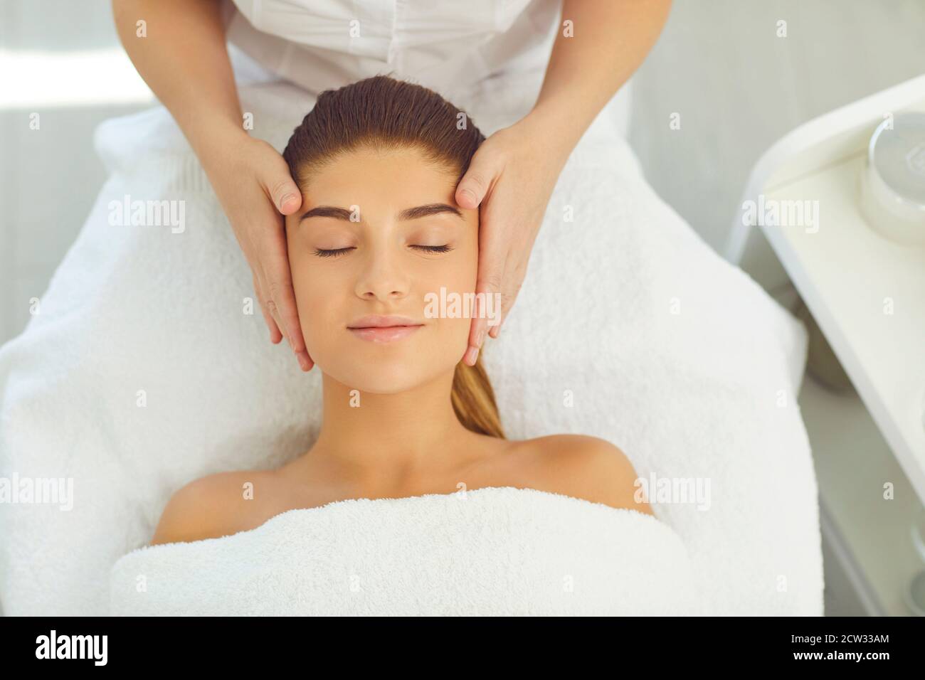 Belle femme recevant un massage du visage couché avec les yeux fermés lit dans le salon de beauté Banque D'Images