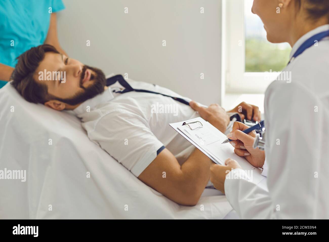 Une jeune femme médecin remplit une carte médicale avec un patient hospitalisé dans une salle d'hôpital. Banque D'Images