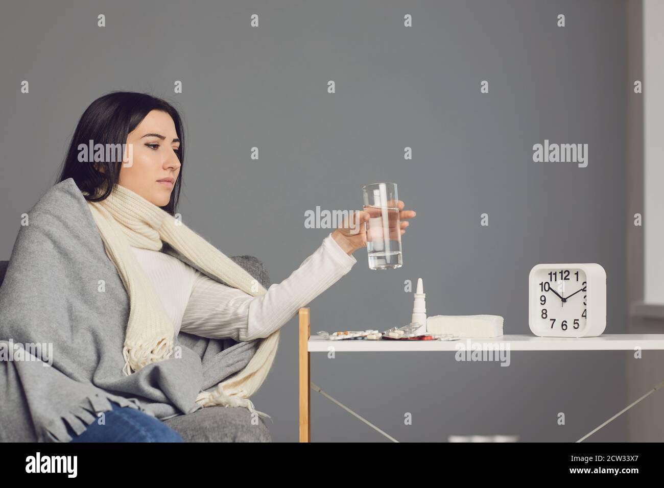 Femme dans une couverture attrapée par le froid et prenant des médicaments contre la grippe, de l'eau potable. Banque D'Images