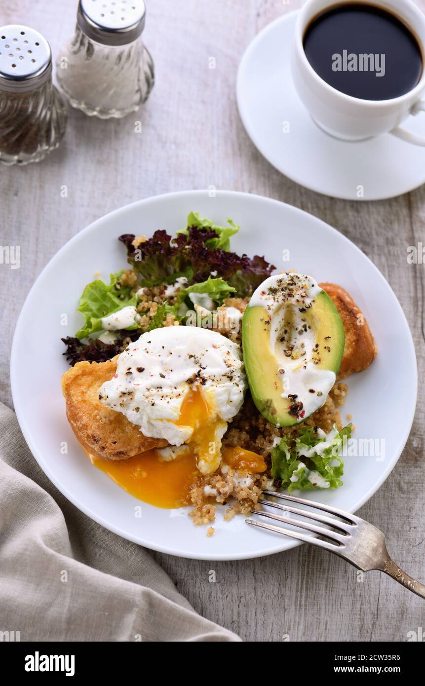 Une assiette de petit déjeuner saine et équilibrée. L'œuf de Benedict se répand sur un toast grillé avec un demi-avocat, un quinoa et une laitue, des épices assaisonnées et du yogu Banque D'Images