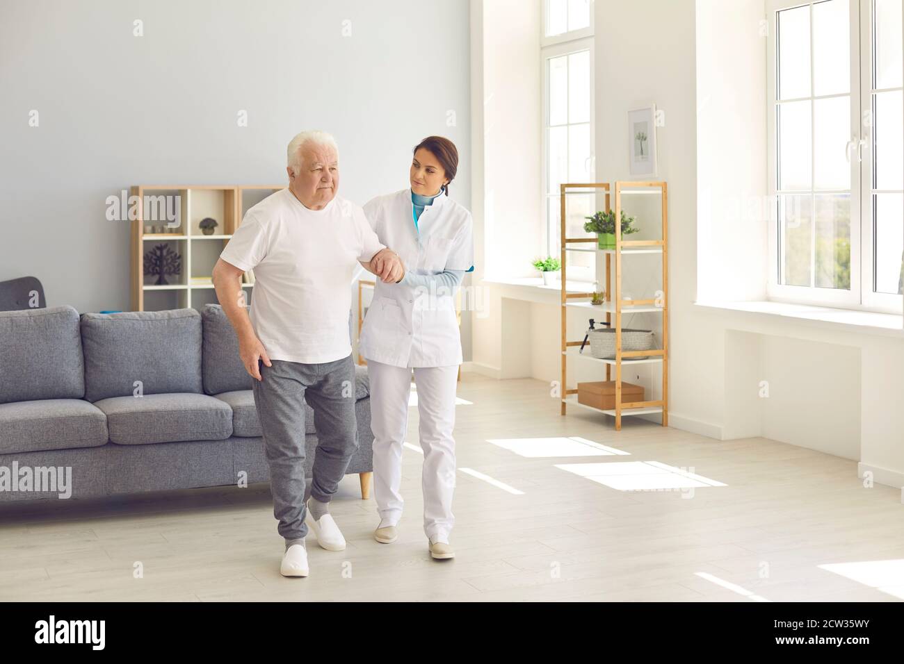 Travailleur de la santé aidant l'homme âgé à marcher dans le bureau de hôpital moderne ou centre de réadaptation gériatrique Banque D'Images