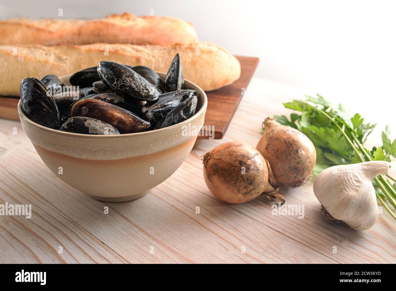 Moules et ingrédients frais crus comme l'oignon, l'ail, le persil et le pain de baguette pour un plat méditerranéen d'apéritif sur une table en bois clair, Copy spa Banque D'Images