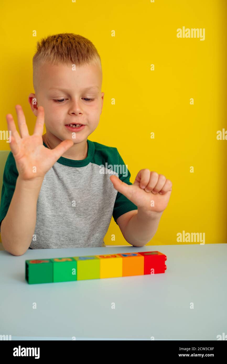 Garçon comptant sur son doigt.sur la table des figures de couleur blocs.on un arrière-plan jaune Banque D'Images