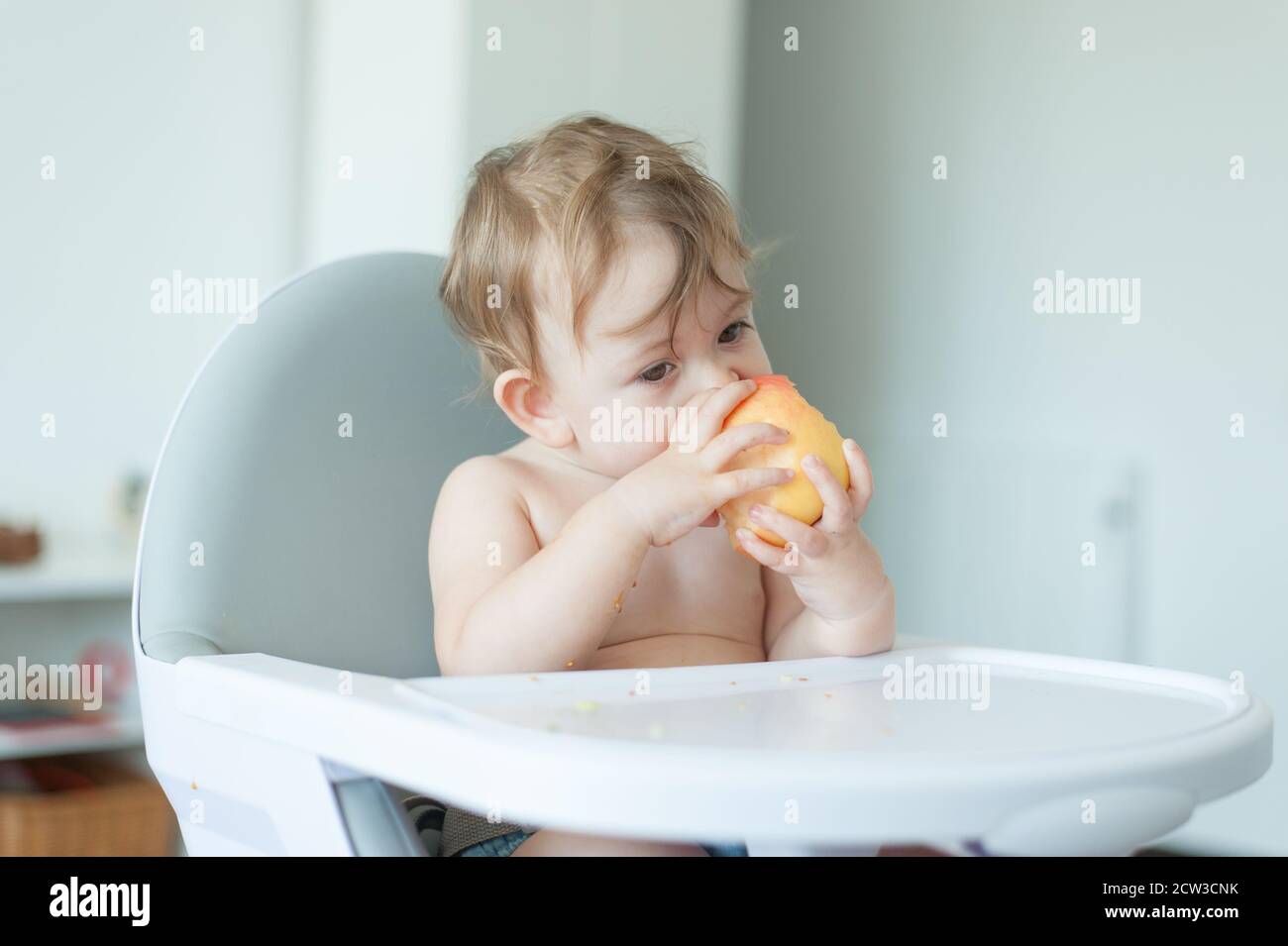 Bébé mangeant une pomme assis sur une chaise haute Banque D'Images