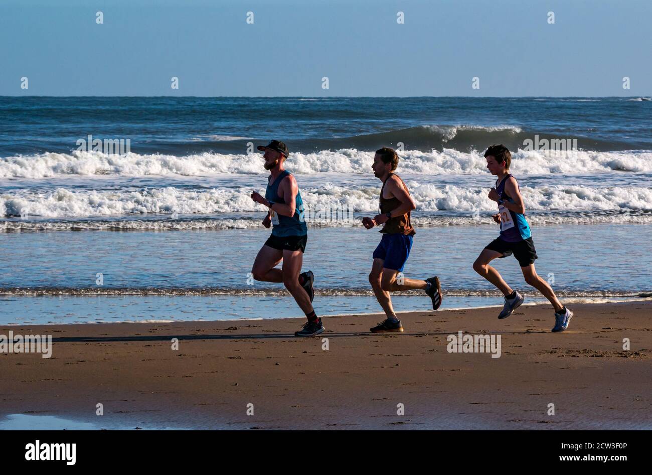 East Lothian, Écosse, Royaume-Uni, 27 septembre 2020. Scurry Running Event : les coureurs participent à un événement de course amusant de la plage de Yellowcraig à North Berwick et de retour sur une belle matinée ensoleillée d'automne. Un trio de coureurs mâles sur la plage de Broadsands avec de grandes vagues en arrière-plan Banque D'Images