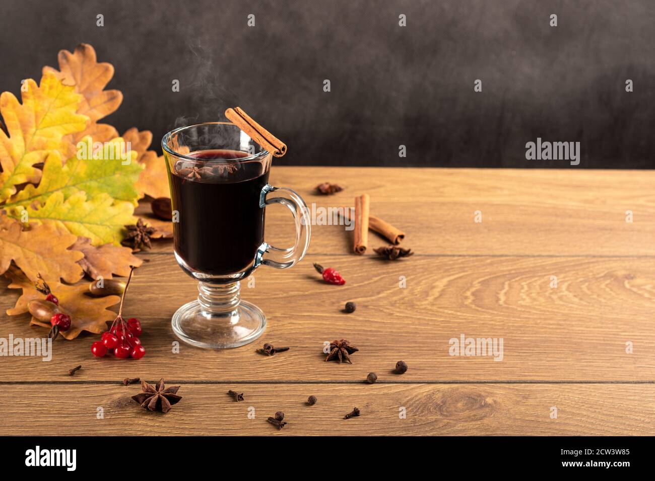 Vin chaud dans des tasses de verre avec de la cannelle et de l'anis sur une table en bois. Fond de feuilles de chêne tombées. Copyspace d'automne Banque D'Images