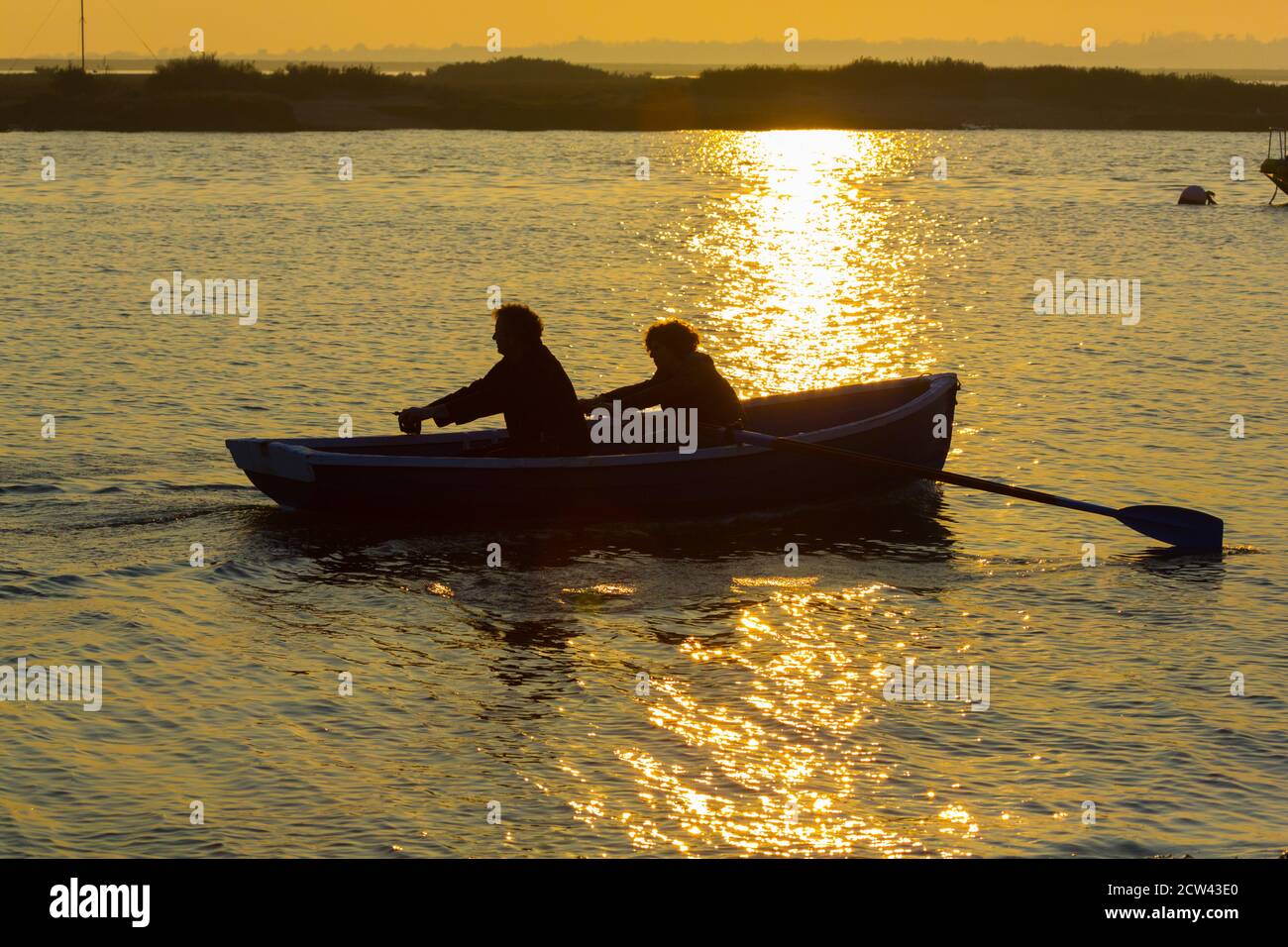 Deux personnes rasant un bateau en mer à West Mersea, Essex, Royaume-Uni Banque D'Images