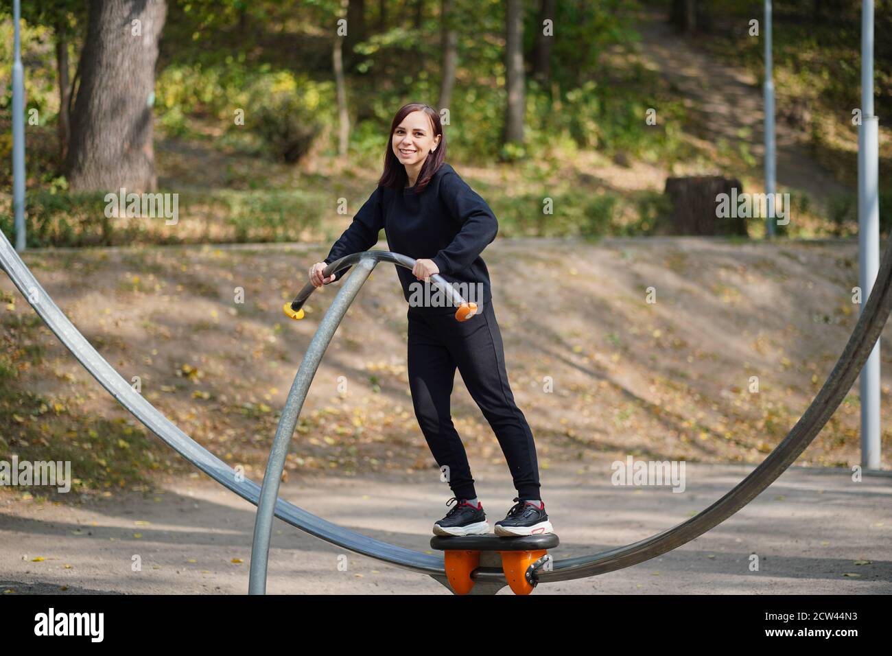 Jeune femme vêtue de vêtements décontractés faisant du sport dans le parc. Femme adulte faisant des exercices sportifs sur simulateur de rue en automne Banque D'Images