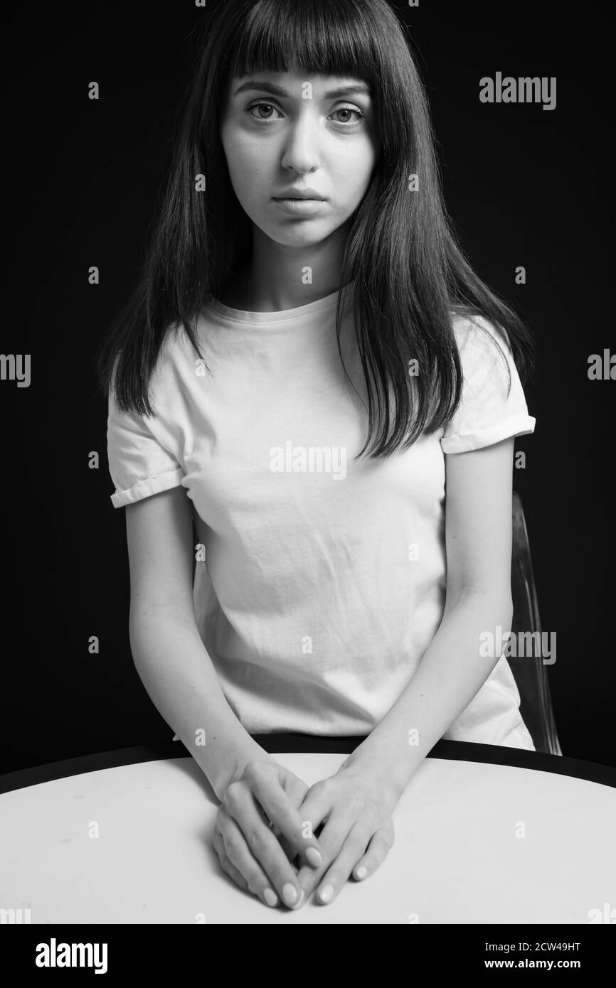 Portrait studio d'une jolie femme brune dans un t-shirt blanc, assis sur un fond noir Uni, regardant l'appareil photo Banque D'Images