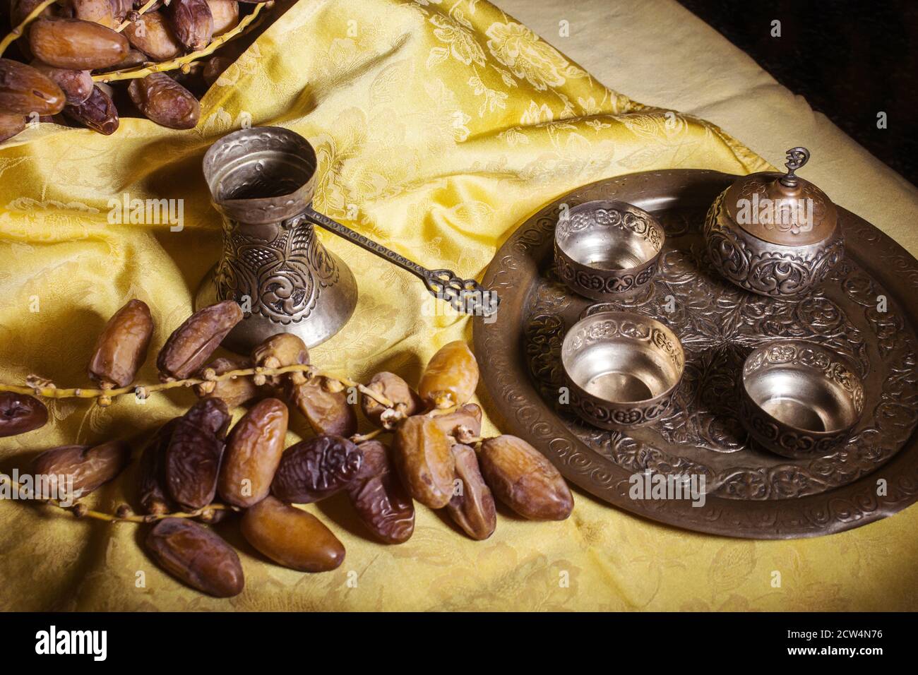 Encore la vie avec Sarajevo ustensiles de café métal sur riche jaune tissu décoré et quelques branches de dates - lumière peinture Banque D'Images