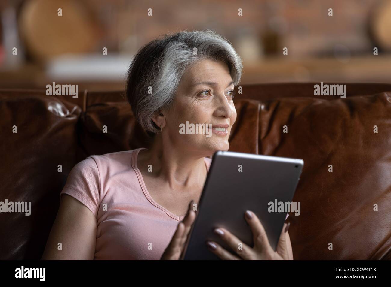 Une femme âgée souriante utilise une tablette pour se détendre à la maison Banque D'Images