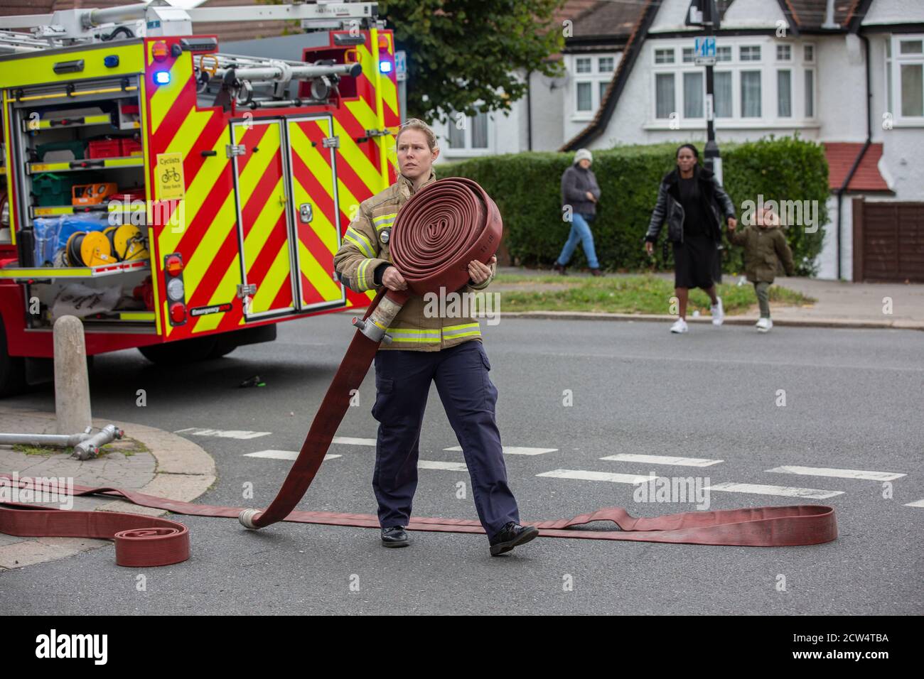 Une pompier lance le tuyau avec la brigade de pompiers de Londres pour assister à un incendie de maison dans une rue résidentielle, sud de Londres, Angleterre, Royaume-Uni Banque D'Images
