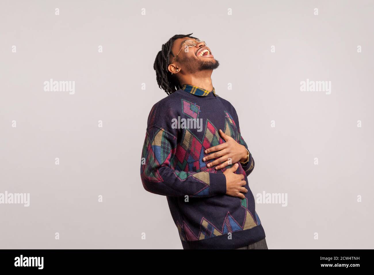 Vue de côté très excitée gars africains heureux avec des dreadlocks riant tenant son ventre avec les mains, blague drôle, anecdote. Prise de vue en studio isolée Banque D'Images