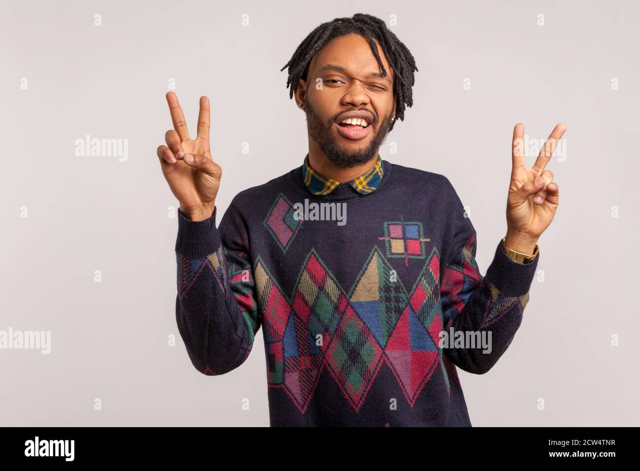 Drôle d'homme africain avec la barbe et les dreadlocks ayant le plaisir de se tordre et de montrer le geste de la paix avec les doigts avec le sourire crasseux sur le visage, taquinant. Salle de studi Banque D'Images