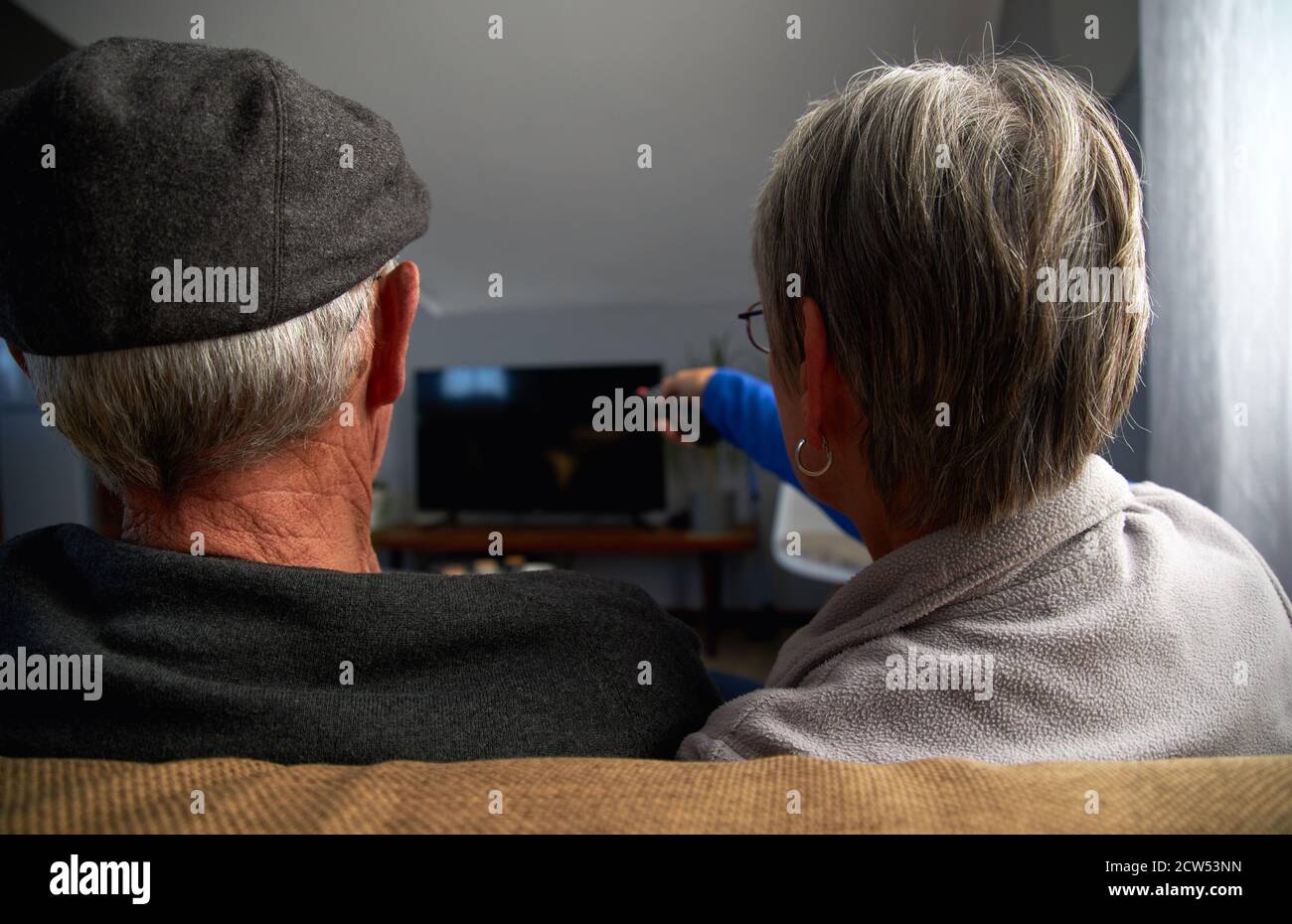 Vue arrière d'un couple senior assis sur un canapé à la maison Regarder la télévision ensemble Banque D'Images