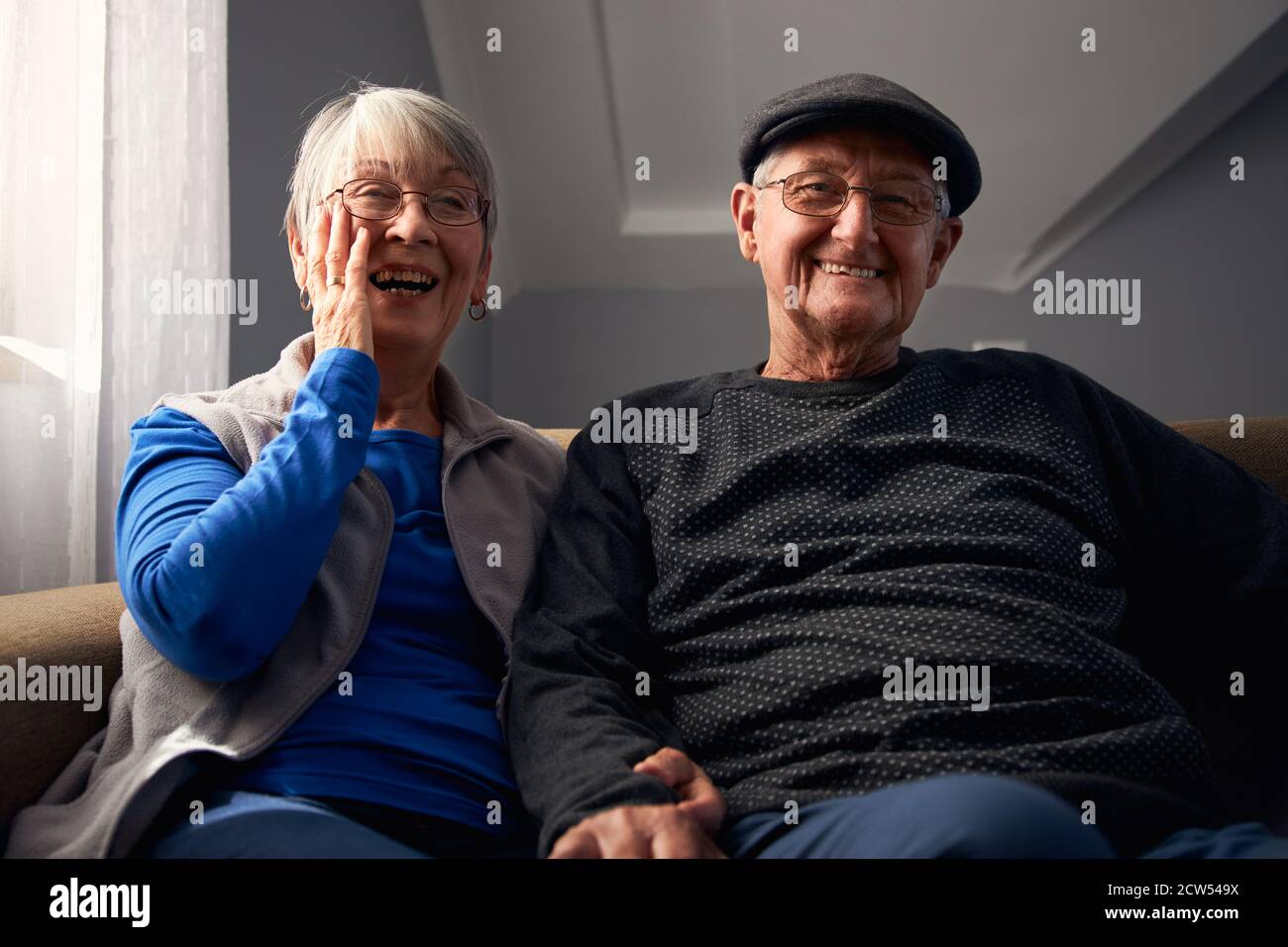 Couple senior souriant assis sur un canapé à la maison regardant la télévision Ensemble Banque D'Images