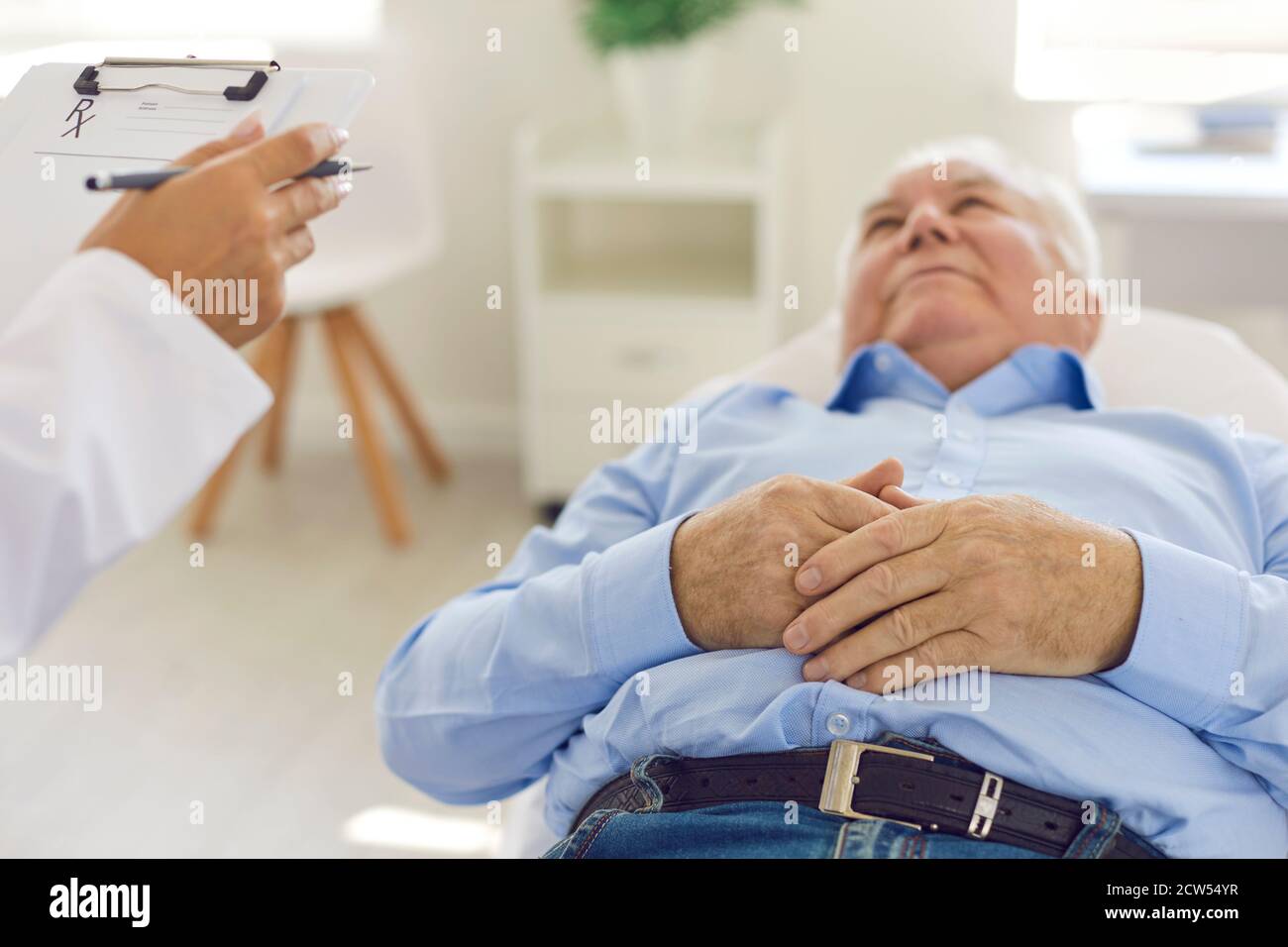 Patient âgé sérieux allongé sur le lit dans le bureau de l'hôpital à l'écoute aux recommandations du médecin Banque D'Images
