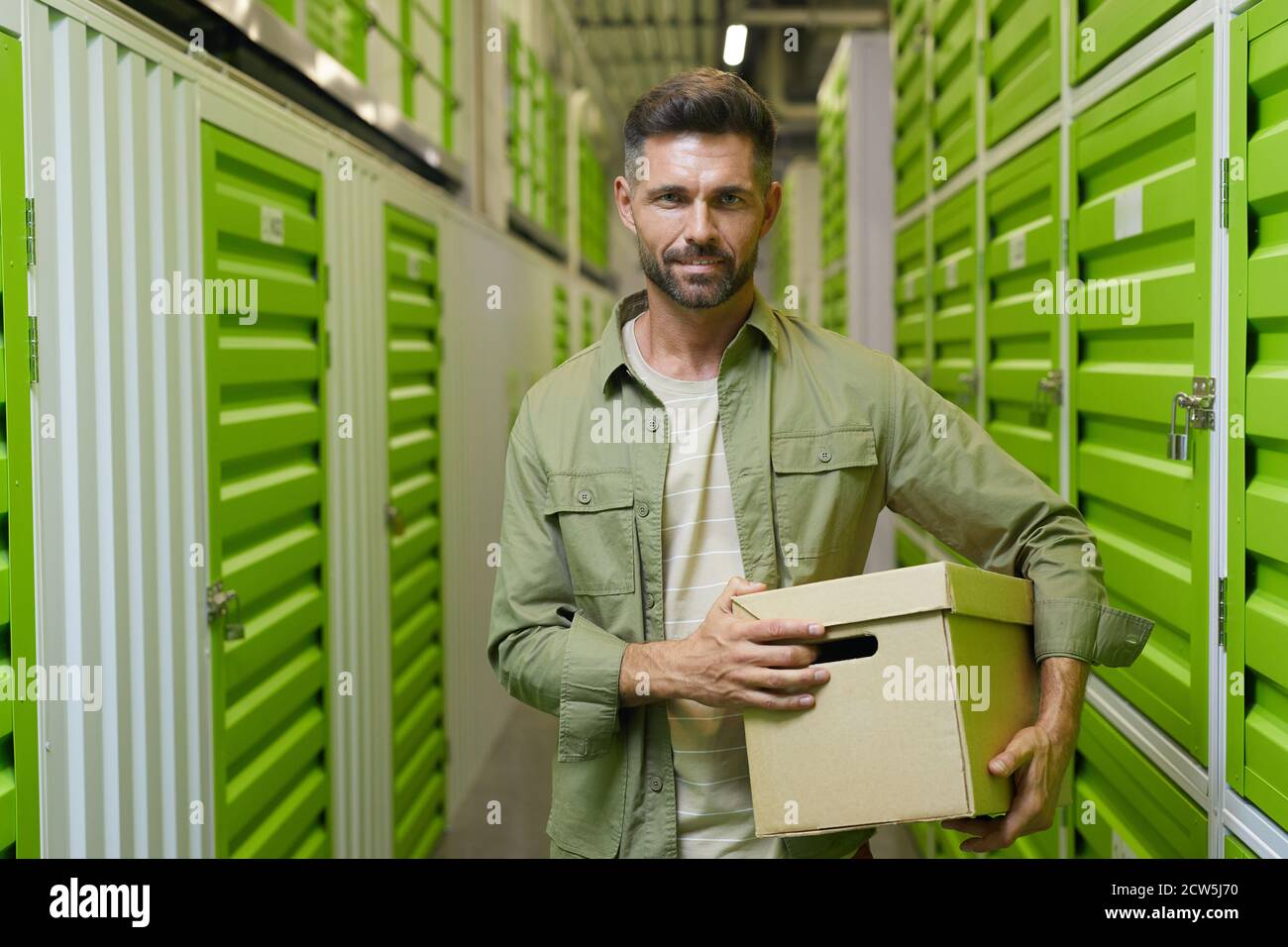 Portrait à la taille du beau homme tenant une boîte en carton debout dans un espace de rangement autonome et regardant l'appareil photo, l'espace de copie Banque D'Images