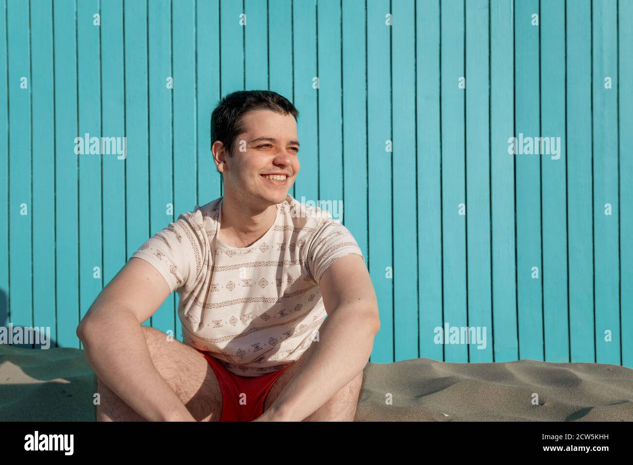 Jeune homme portant un pantalon de maillot de bain souriant sur une plage de  sable dim Photo Stock - Alamy