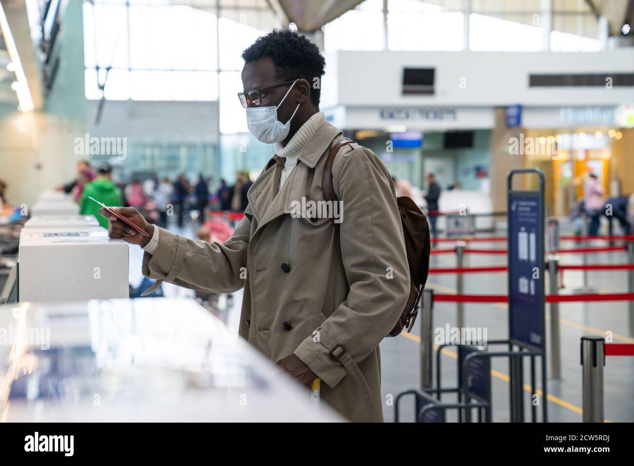 Un homme afro-américain se tient aux comptoirs d'enregistrement du terminal de l'aéroport, donnant un passeport à un agent. Règles de vol pendant une pandémie Covid-19 uniquement Banque D'Images