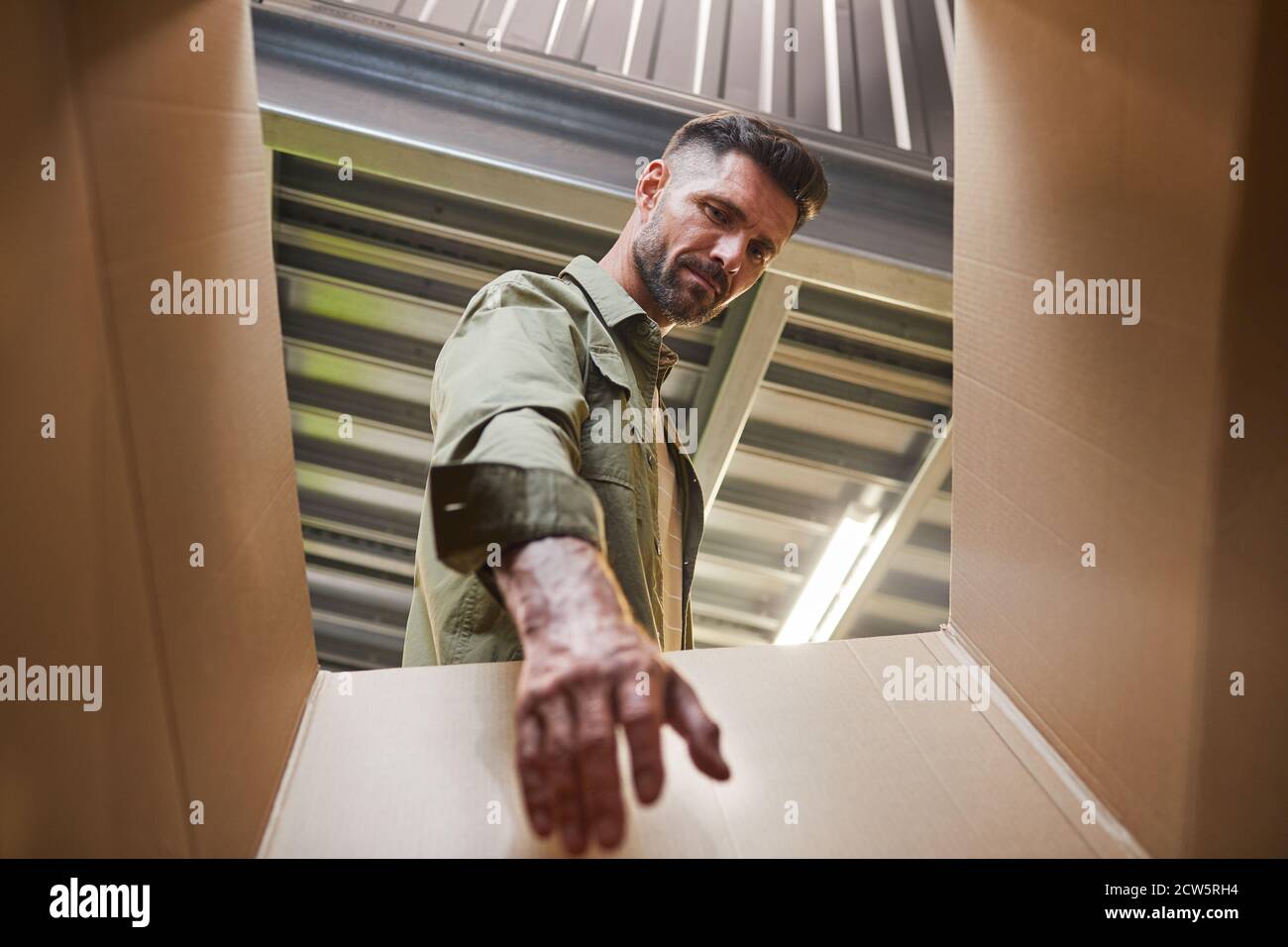 Prise de vue en angle bas à la jolie boîte de transport de l'homme barbu lors du chargement de l'unité d'auto-stockage, espace de copie Banque D'Images