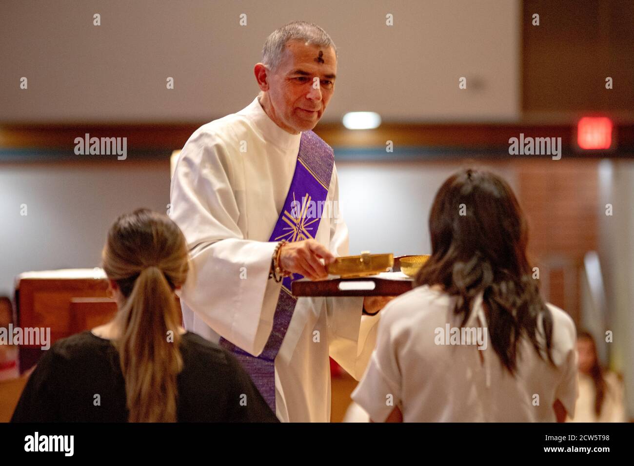 Un diacre rodé avec une croix de cendre sur son le front distribue des bols de cendre à des assistantes d'autel pendant Services de mercredi de cendres dans un Southern Cal Banque D'Images