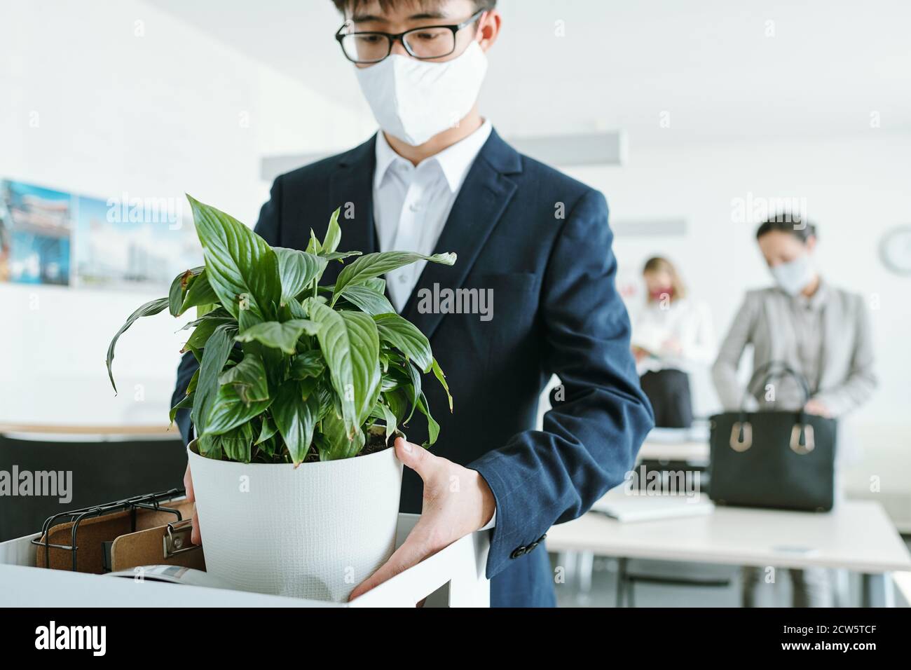 Jeune homme d'affaires asiatique en tenue de cérémonie et masque de protection à retirer pot de fleurs Banque D'Images