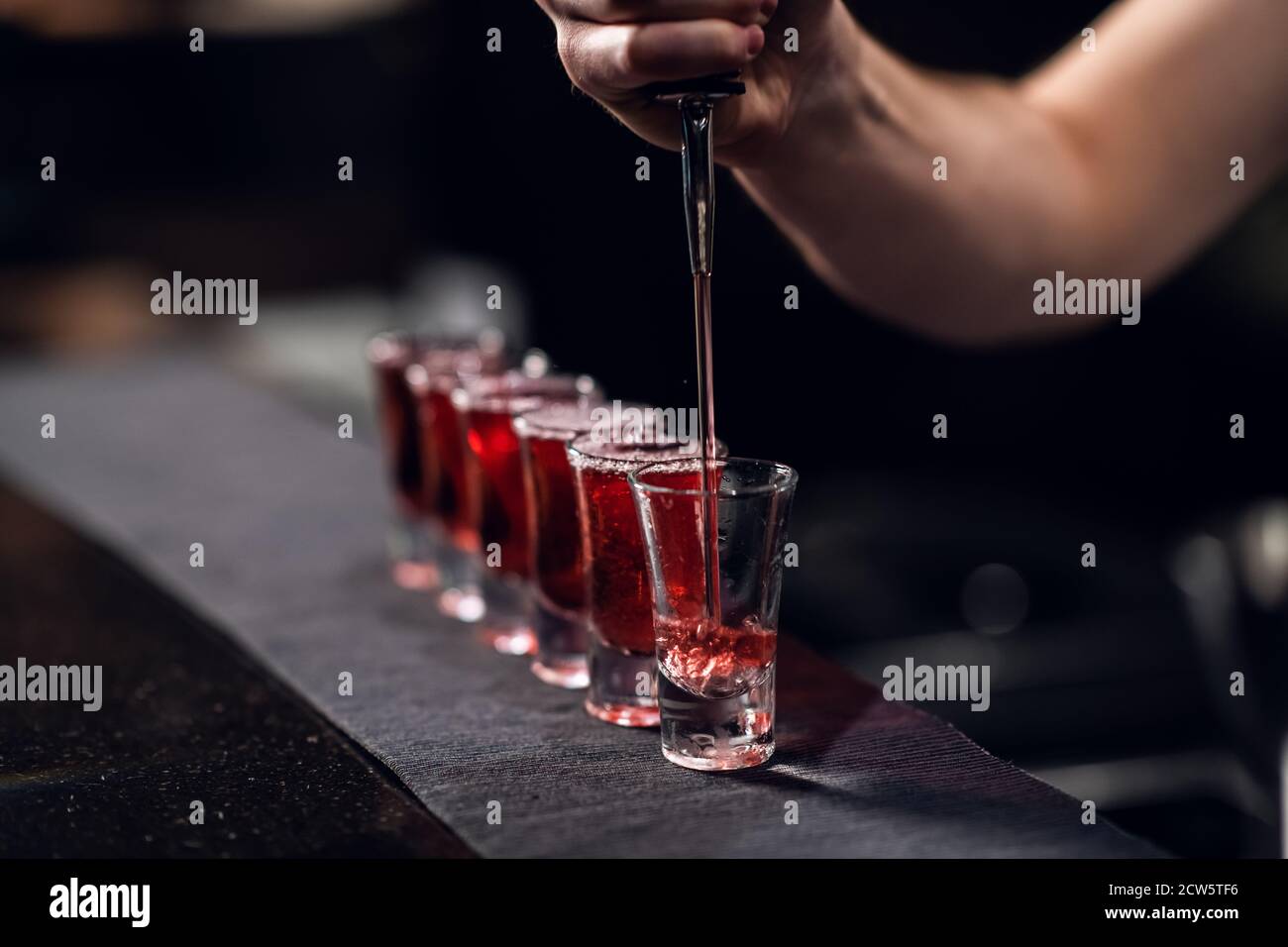 le barman remplit les prises de vue avec de la liqueur rouge provenant d'une bouteille sur le bar. Banque D'Images