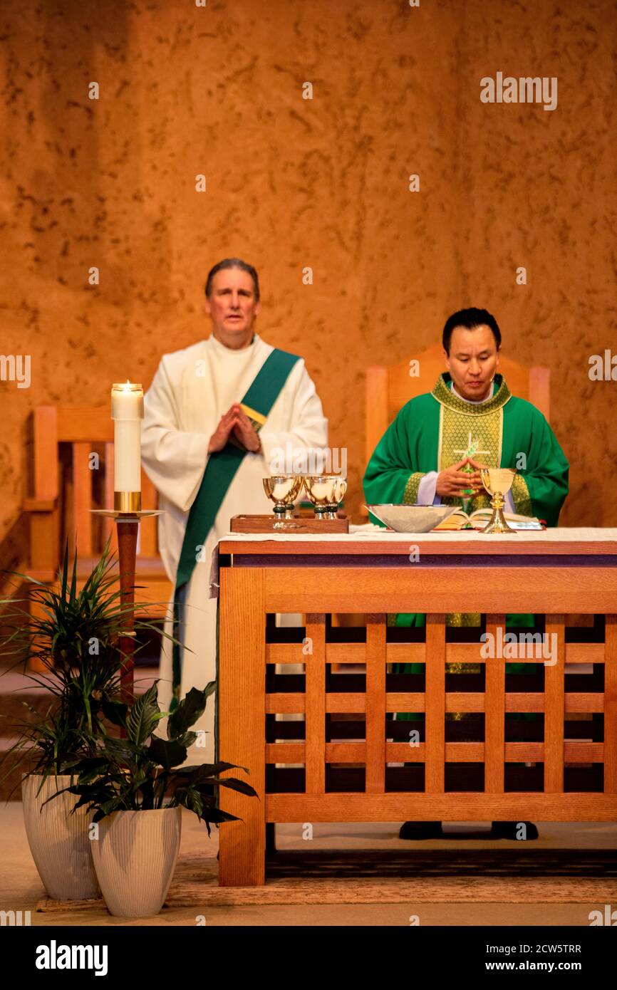 Un diacre rodé et un prêtre américain d'Asie célèbrent la messe sur l'autel d'une église catholique de Californie du Sud. Notez les gobelets pour le vin sacramentel. Banque D'Images