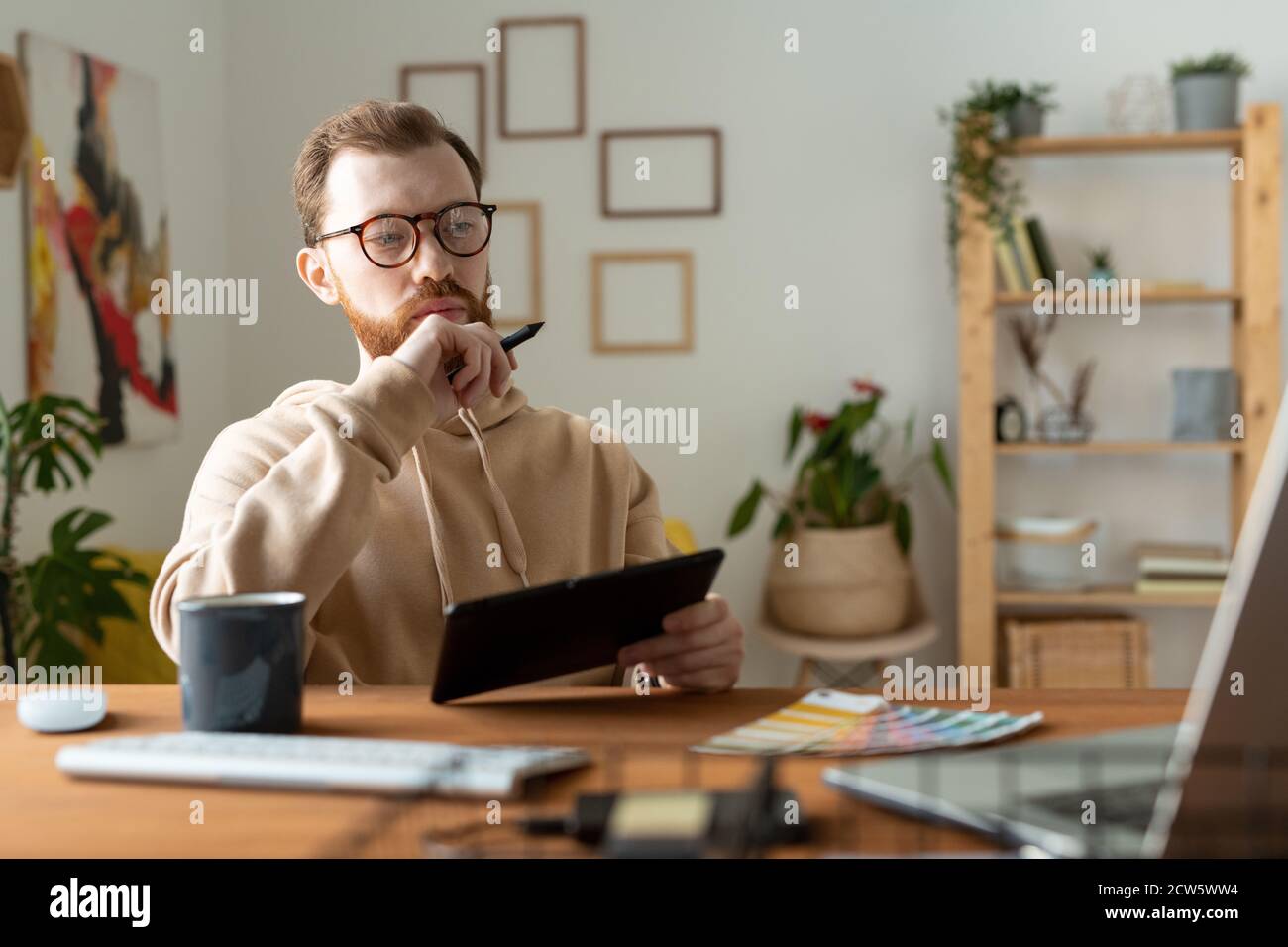 Jeune designer freelance pensif à barbe regardant l'écran d'ordinateur portable pendant dessin Banque D'Images