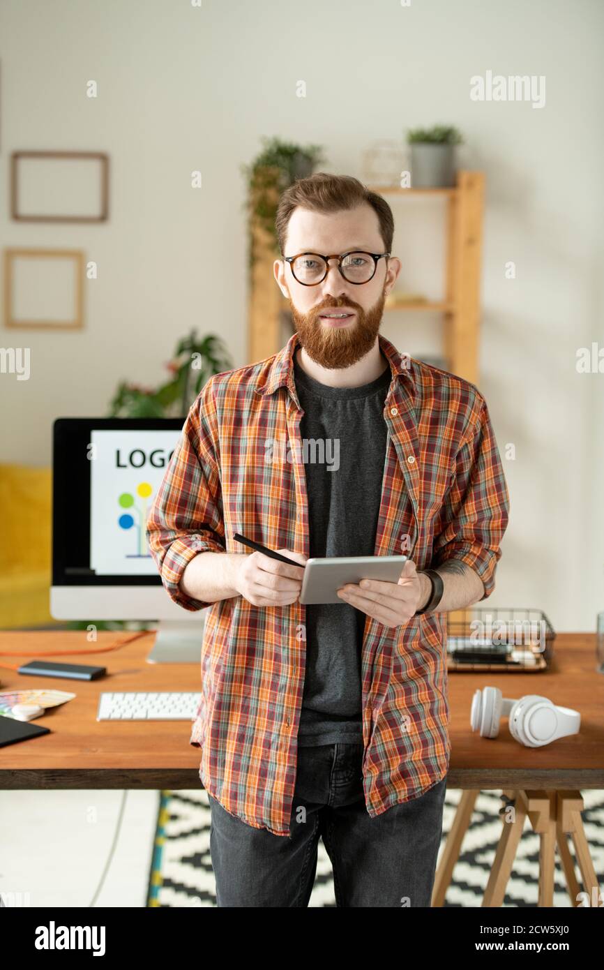 Jeune créateur barbu utilisant une tablette et un stylet contre un ordinateur moniteur Banque D'Images