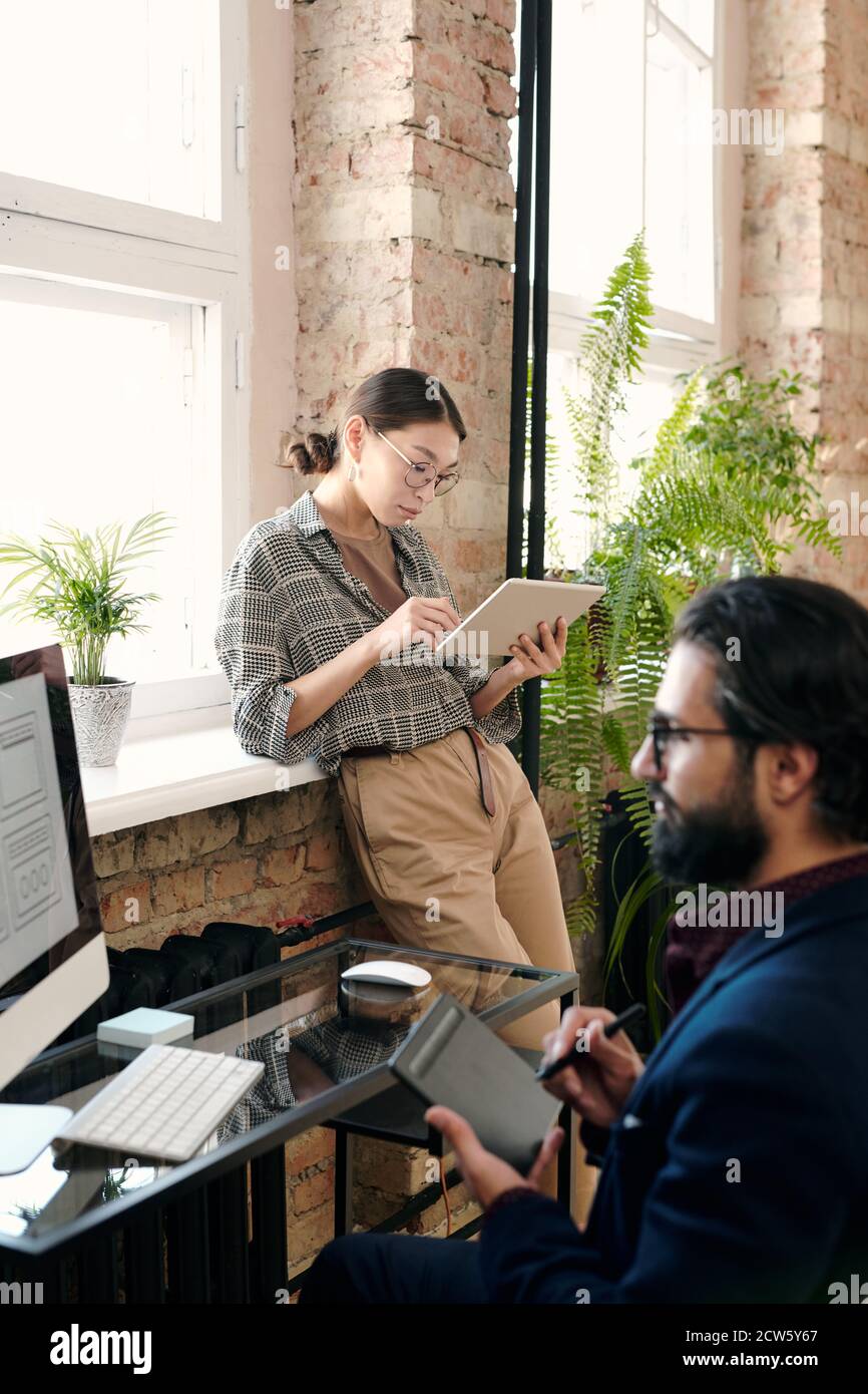 Jeune designer féminine utilisant une tablette numérique pendant que sa collègue dessine esquisse Banque D'Images