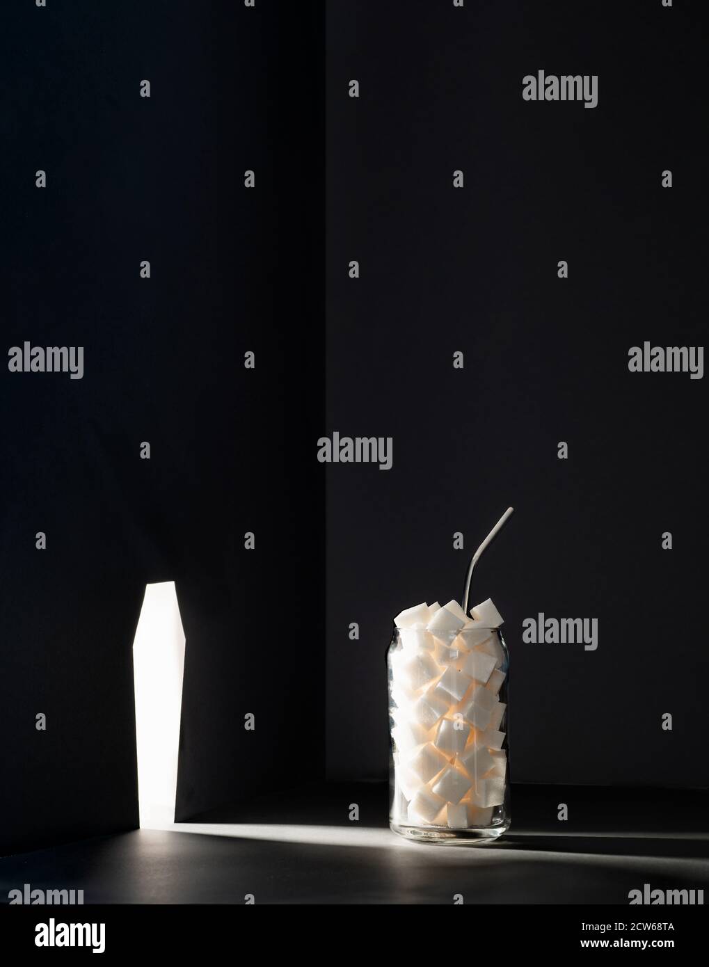 La maladie de diabète, l'insulinorésistance, la dépendance au sucre, novembre 14 est la journée de sensibilisation au diabète et les sucres ajoutés vous tuent concept. Bol en verre avec cubes de sucre illuminé par la fente de cercueil Banque D'Images