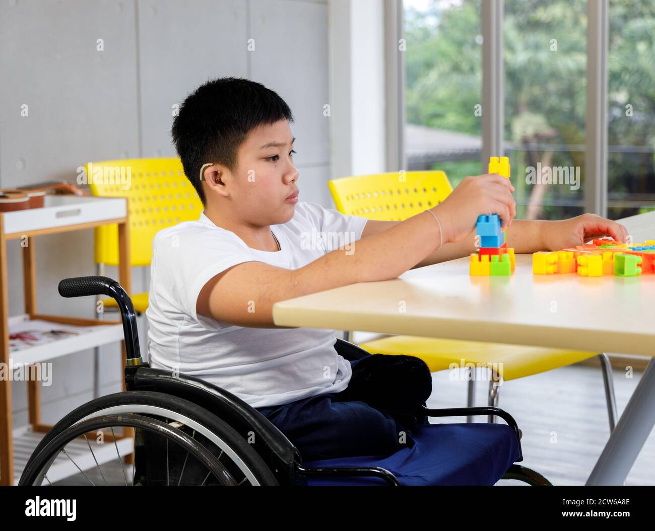 Un garçon handicapé en fauteuil roulant joue un puzzle coloré en classe. Concept d'apprentissage des enfants handicapés à l'école. Banque D'Images