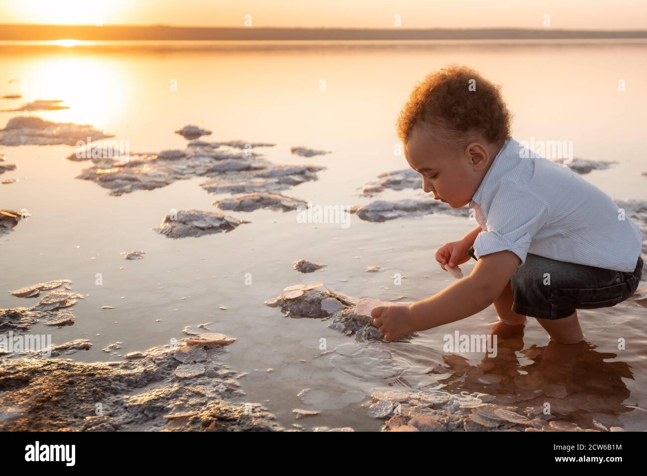 Mignon Melange Race Bebe Garcon Regarde Les Cristaux De Sel Avec Interet Petit Enfant Curieux Charmant Enfant Curly Jouant Sur La Plage De L Estuaire Photo Stock Alamy