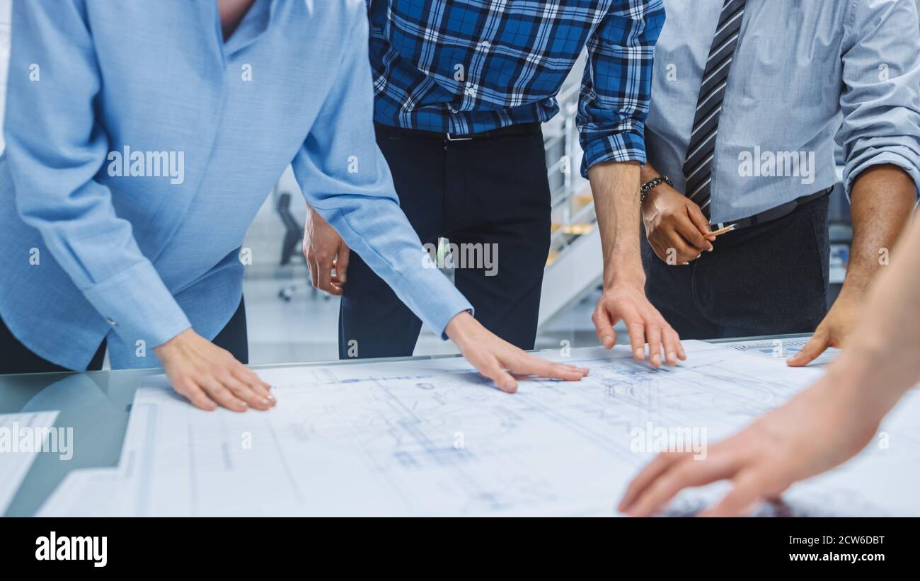 Dans le centre d'ingénierie industrielle : divers groupes d'ingénieurs et de techniciens réunis autour de la table démêle les feuilles de conception de moteur Banque D'Images