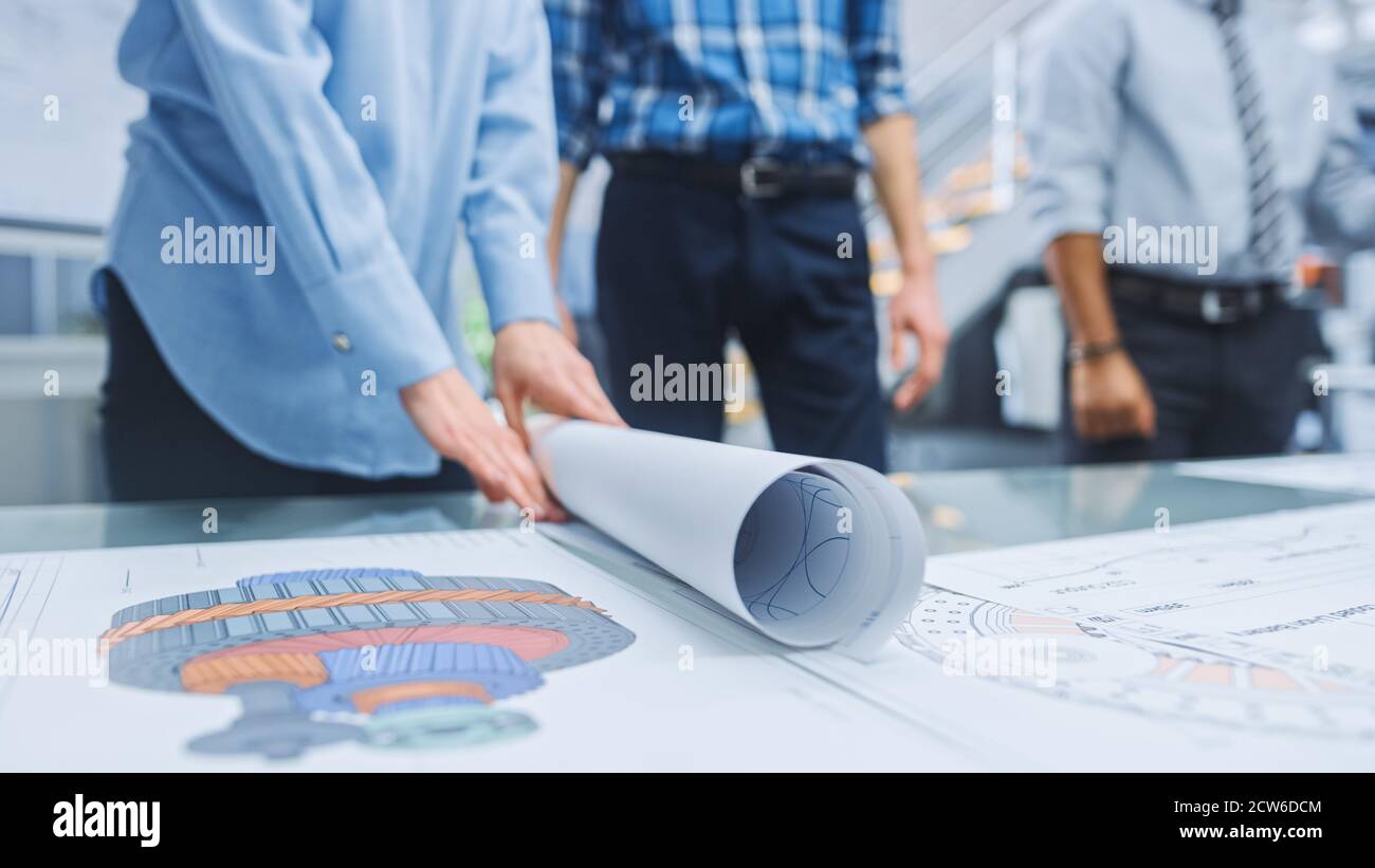 Dans le centre d'ingénierie industrielle : divers groupes d'ingénieurs et de techniciens réunis autour de la table démêle les feuilles de conception de moteur Banque D'Images