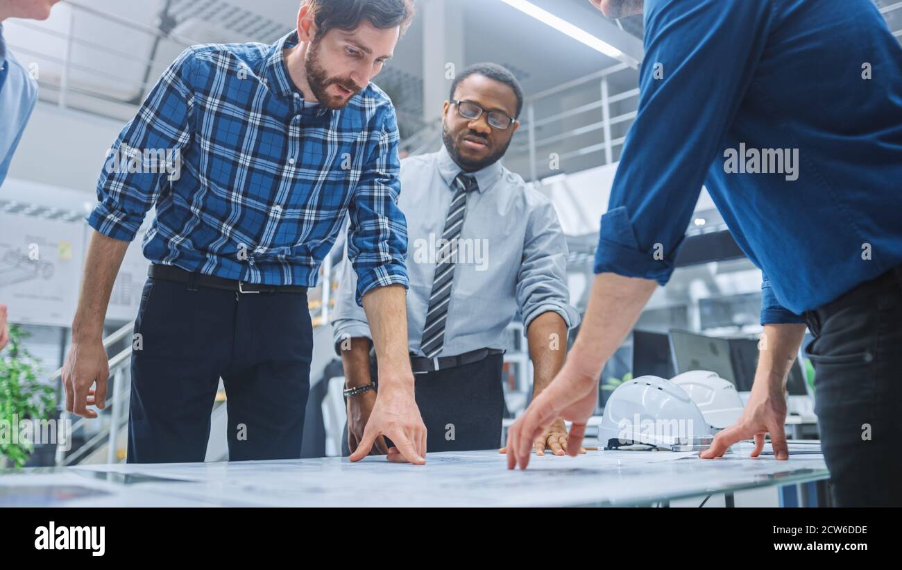 Dans le centre d'ingénierie industrielle : divers groupes d'ingénieurs et de techniciens réunis autour de la table démêle les feuilles de conception de moteur Banque D'Images