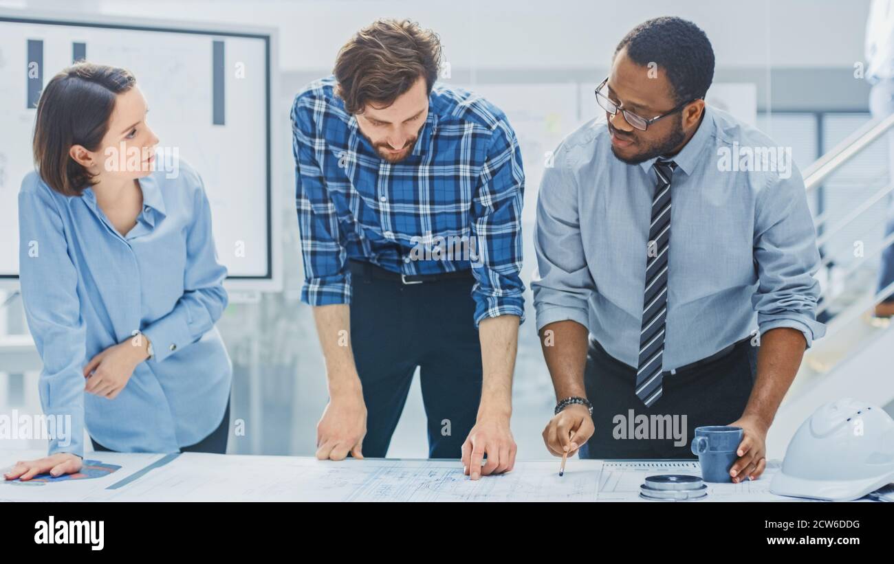 Dans le centre d'ingénierie industrielle : divers groupes d'ingénieurs et de techniciens réunis autour de la table démêle les feuilles de conception de moteur Banque D'Images