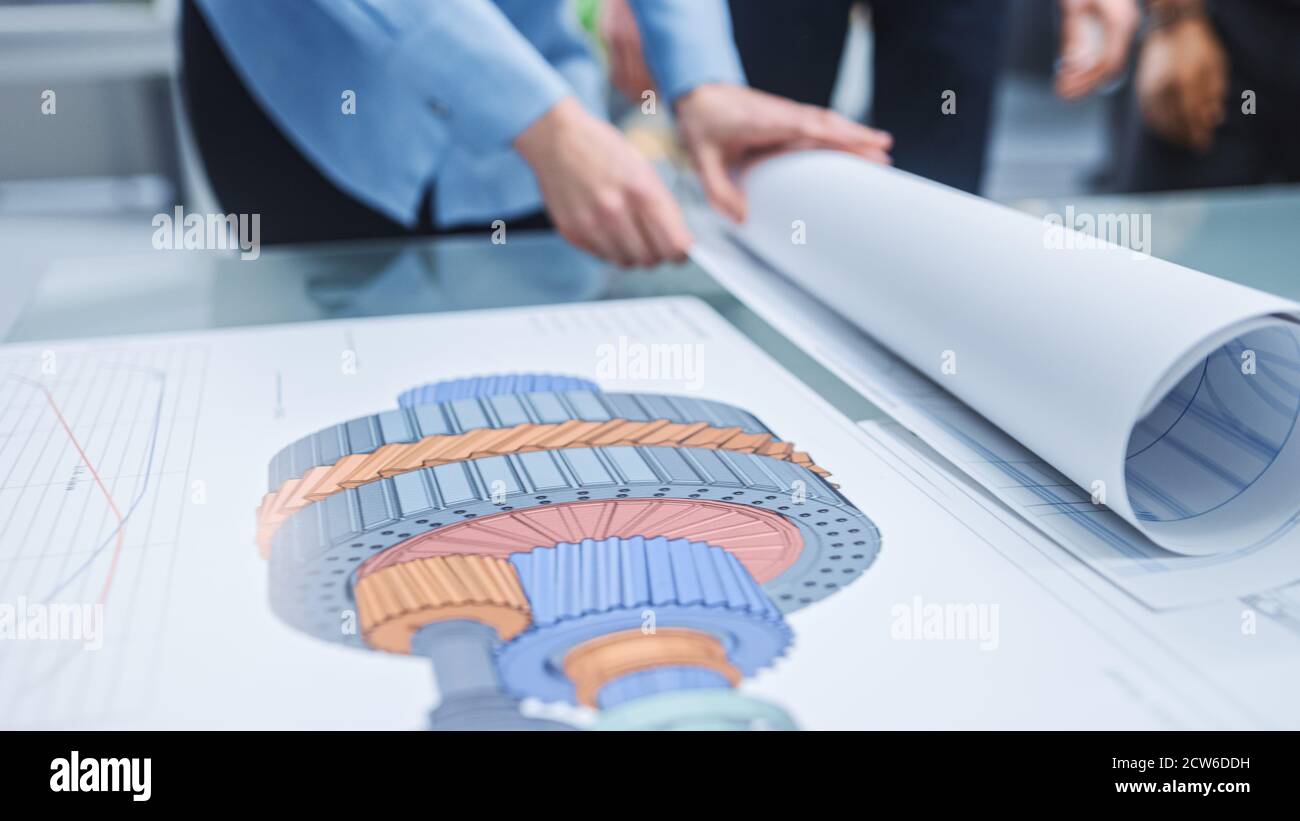 Dans le centre d'ingénierie industrielle : divers groupes d'ingénieurs et de techniciens réunis autour de la table démêle les feuilles de conception de moteur Banque D'Images