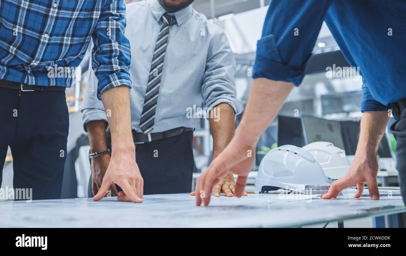 Dans le centre d'ingénierie industrielle : divers groupes d'ingénieurs et de techniciens réunis autour de la table démêle les feuilles de conception de moteur Banque D'Images
