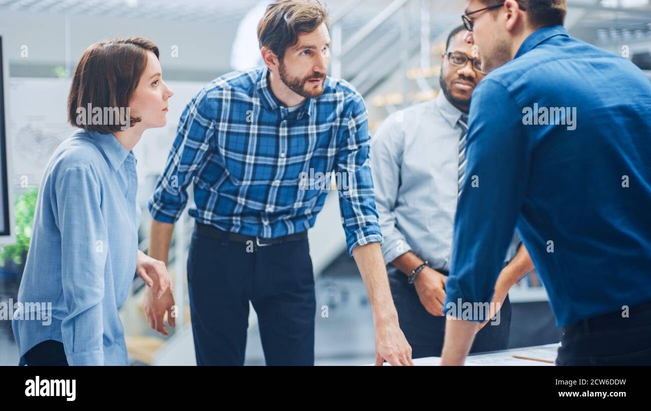Dans le centre d'ingénierie industrielle : divers groupes d'ingénieurs et de techniciens réunis autour de la table démêle les feuilles de conception de moteur Banque D'Images